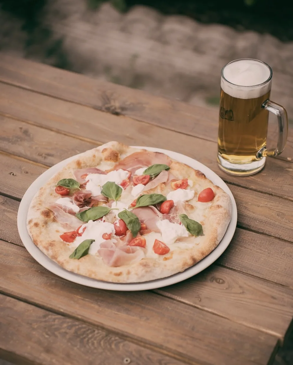 Pizza con crudo e stracciatella accanto a una birra nel dehors di The Cave
